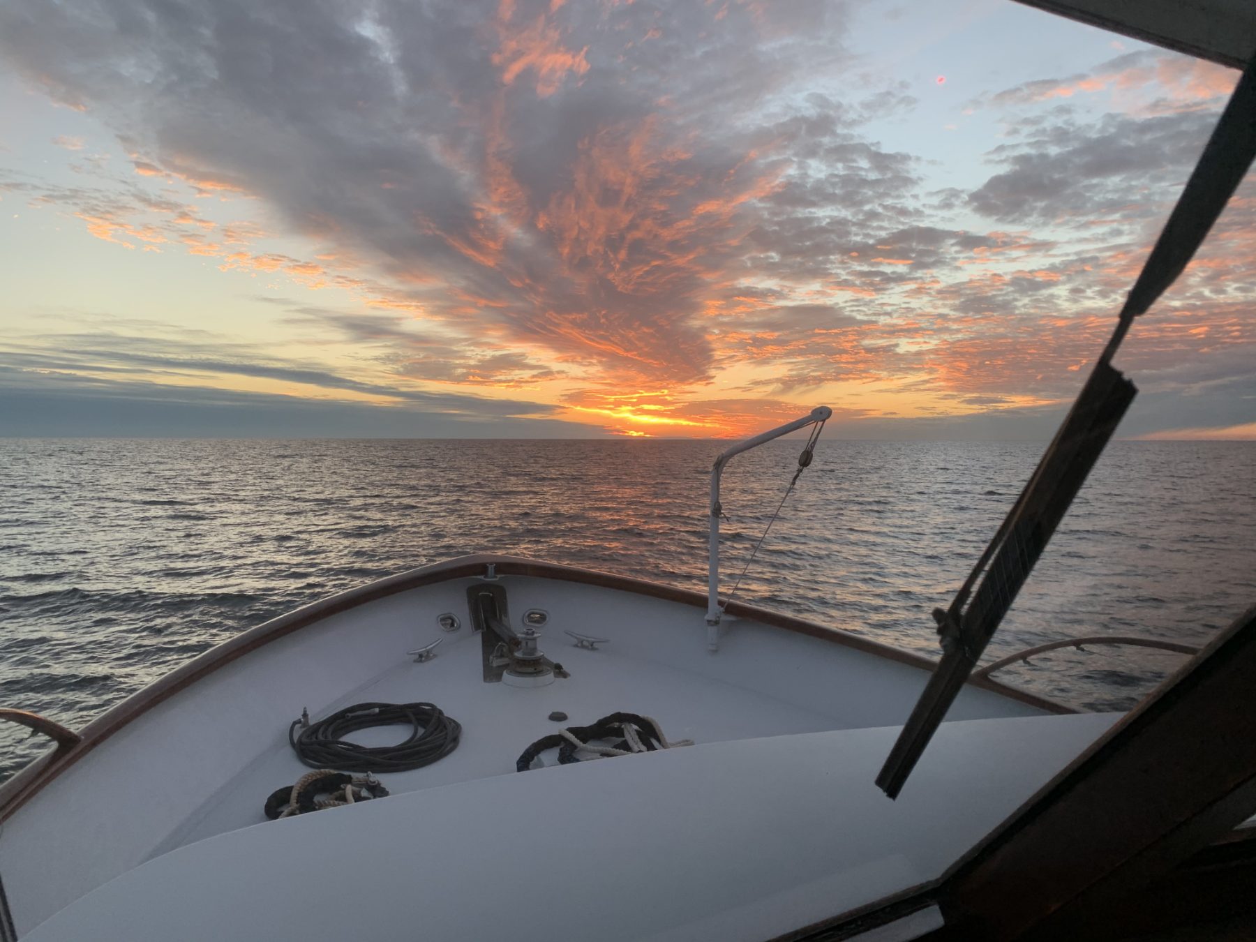 The bow of the motor yacht Freeplay under way toward a sunset on open water.