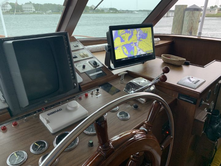 The helm of a motor yacht with a chartplotter, gauges and a wooden wheel.