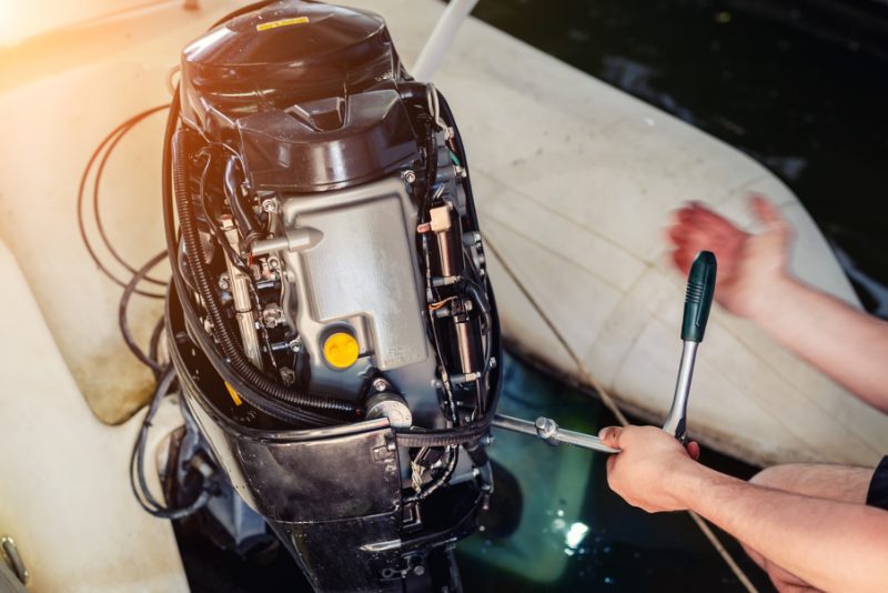 Hands with a wrench working on an outboard motor with its cowling removed.